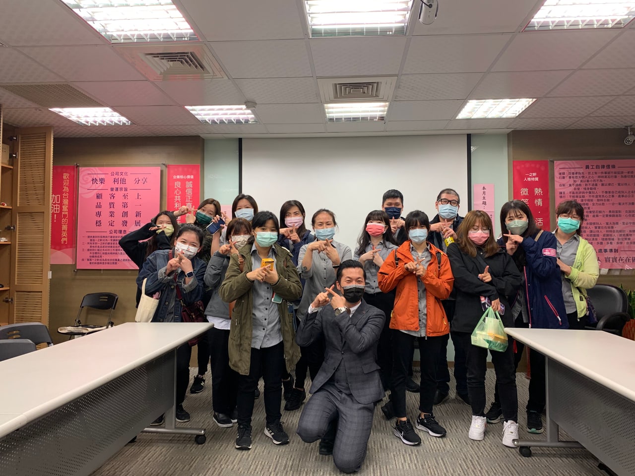 「門市服務失誤補救課程」結業合照：李奕勳與十餘位學員一起比出手指姿勢，背景是公司文化與員工自律信條海報